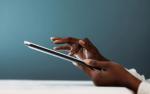 Close-up of a person’s hands using a digital tablet, with fingers gently tapping the screen against a soft blue background.